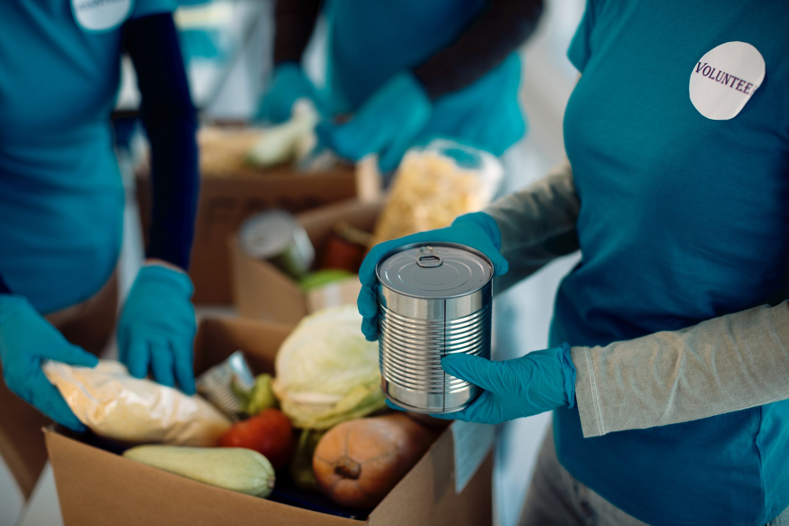 unrecognizable volunteers packing donated food inside cardboard boxes
