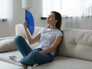 Woman suffers from unbearable hot weather waving fan cooling herself