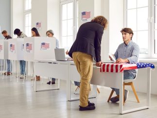 Back view portrait of a man registering at polling station with American flags on election day.