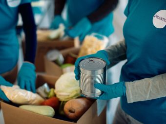 unrecognizable volunteers packing donated food inside cardboard boxes